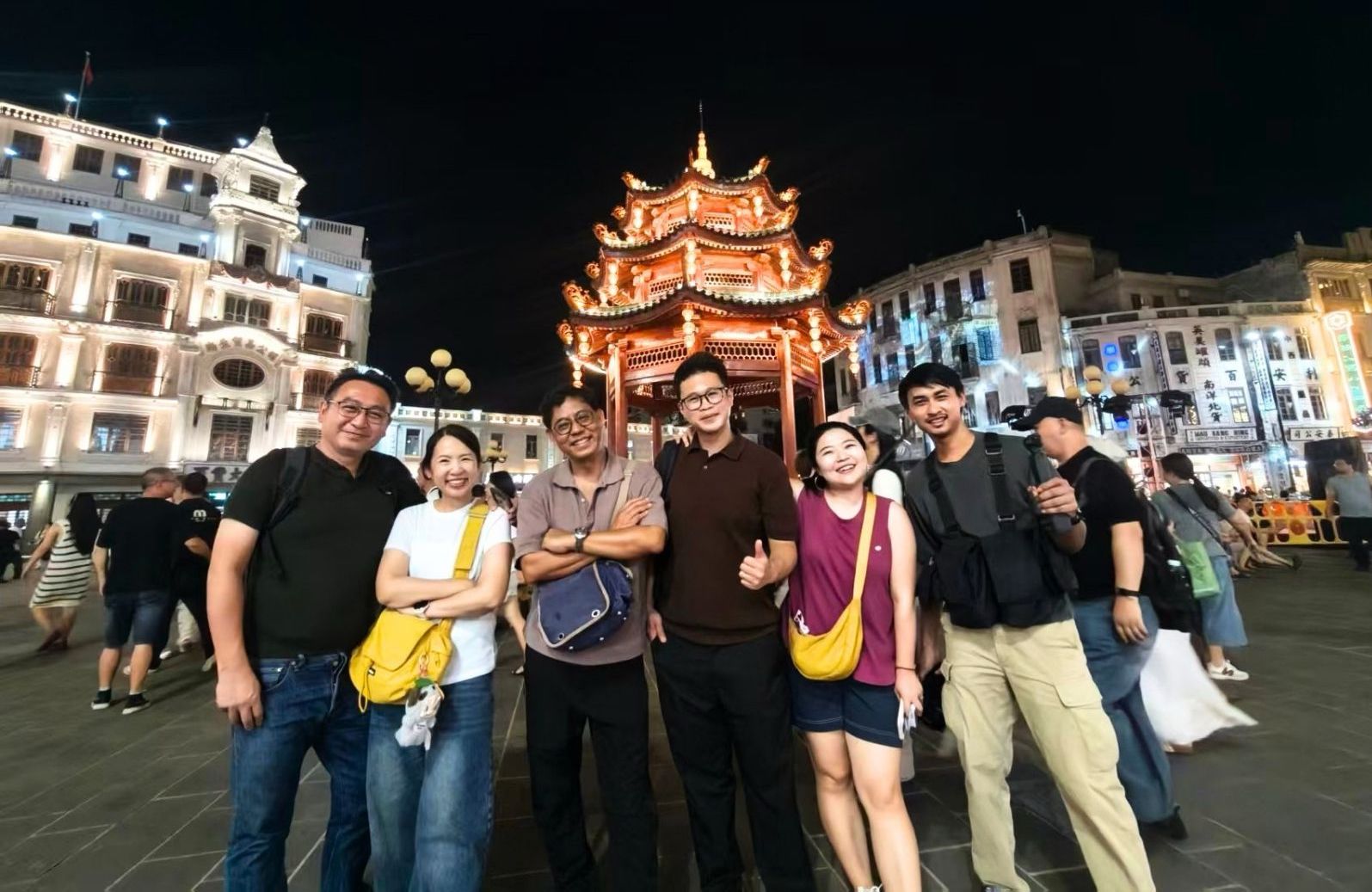 a group of people standing in front of a Chinese pavillion at night in Xiaogongyuan, Shantou